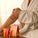 A person in a white robe applying Tropic’s Spiced and Citrus body care products to their legs, with two bright orange and red tubes and matching gift packaging displayed on the bed.